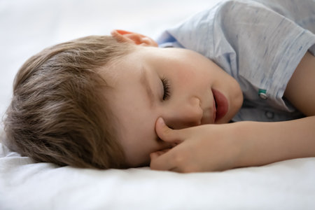 Close up 7s Caucasian boy sleeping on cozy bed, white comfortable mattress, calm cute child kid with closed eyes resting, taking day nap, relaxing resting alone, childhood and sleep conceptの写真素材