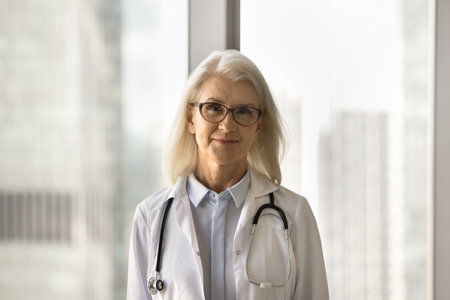 Positive senior medical therapist woman in glasses and white coat head shot portrait. Female doctor, healthcare professional with stethoscope looking at camera, promoting clinical checkupの写真素材