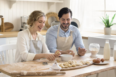Happy smiling spouses make dough for homemade pastries, cooking together in modern kitchen, enjoy joint hobby, laugh, spend weekend at home, preparing for family holiday event. Relationship, culinaryの写真素材