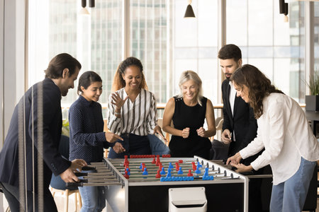 Happy diverse team of business friends meeting at funny board game in office lobby, modern...