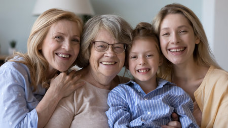 Happy pretty girl kid, young, mature, elderly women standing close, hugging, looking at camera, posing with toothy smiles. Four female family generations meeting head shot portrait. Banner shotの写真素材