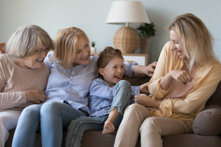 Cheerful excited loving great grandma, grandmother, daughter kid tickling happy young mom, laughing, shouting, playing funny games on couch, enjoying activity, closeness, family leisureの写真素材