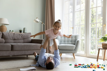 Happy little preschool kid playing active game with dad, doing acroyoga, making airplane with open arms, laughing, enjoying activity, leisure time with father. Daddy lying on floor, lifting childの写真素材