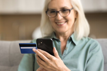 Close up of smartphone and credit card in female hands. Happy senior lady using financial commercial application, online banking service, shopping on Internet on mobile phone. Cropped shotの写真素材