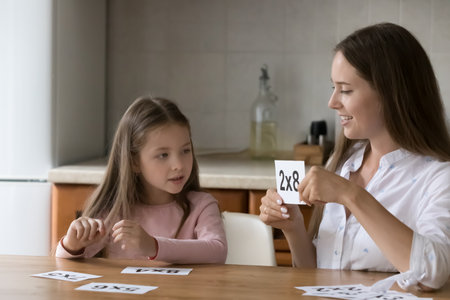 Engaged caring mother helping little daughter with learning math, doing school homework, multiplication table, using flash cards, playing mathematic game. Schoolchild home education conceptの写真素材