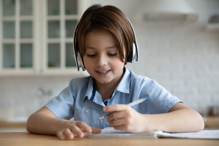 Close up smiling 7s boy in headphones writing taking notes, studying online at home, happy child kid student listening to lecture or watching webinar, homeschooling and distance learning conceptの写真素材