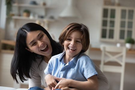Overjoyed Asian mother and little son hugging and laughing, spending leisure time at home together, excited happy young mom with 7s child kid having fun, tickling and cuddling, enjoying weekendの写真素材