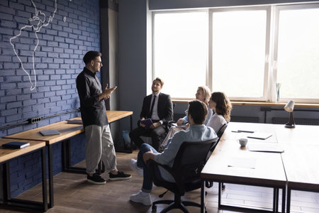 Young creative manager lead corporate meeting with employees explains tasks, discussion of sales...