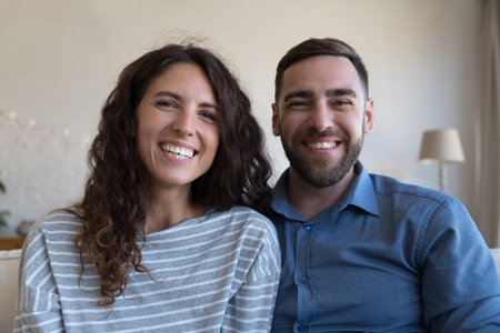 Happy joyful dating couple home head shot portrait. Husband and wife sitting close, looking at...