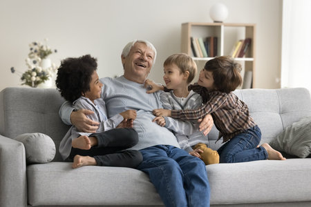 Happy multigenerational family enjoy playtime sit on sofa at home. Three adorable multiethnic...