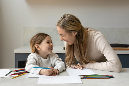 Cheerful mom and happy laughing kid having fun, drawing together at home, talking, chatting,...