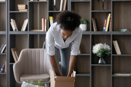 Young African American woman, millennial girl, receiving order from internet store, opening carton...