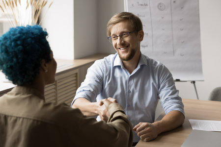 Positive confident businessman giving greeting handshake to female client. Multiethnic business partners, colleagues shaking hands at workplace, smiling, ending successful meetingの写真素材