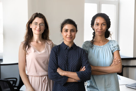 Happy confident beautiful diverse businesswomen standing together in office, looking at camera,...