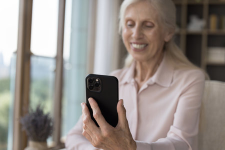 Happy retired woman enjoy videocall via application on smartphone, close up. Smiling elderly female staring at cellphone screen, start conversation use app, having virtual meeting with family use techの写真素材