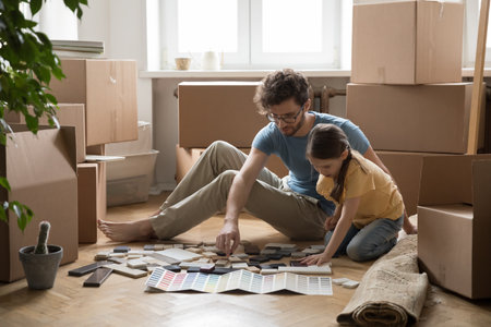 Young father and little daughter sit on floor choosing samples for house decoration, review colorful swatches start renovation of new apartment. Relocation of young family to own flat, repair worksの写真素材