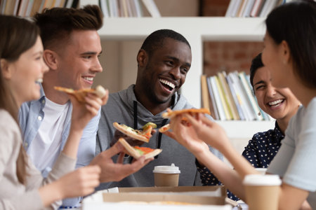 Overjoyed multiracial students friends have fun joke eating delicious pizza during lunch break,...