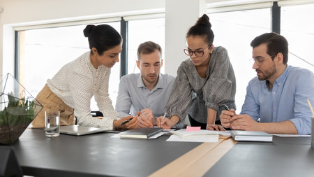 Serious diverse multiracial colleagues coworkers work together on paperwork at meeting in office. Focused multiethnic employees brainstorm discuss documents at briefing. Teamwork, cooperation concept.の写真素材