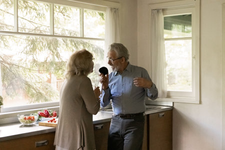 Having fun at kitchen. Happy elderly married couple enjoy cook together at home sing by music use...