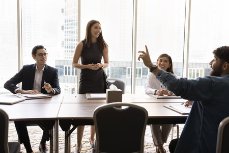 Happy Latin project manager woman holding brainstorming with colleagues in office boardroom....