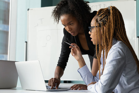 I have question. Black woman teacher stand by desk of mixed race female student look on pc screen...
