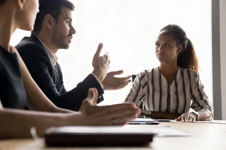 Motivated businessman sharing ideas for team brainstorming, talking to colleagues at meeting tale, explaining offer, management strategy. Diverse business group working togetherの写真素材