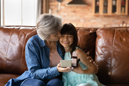 Happy birthday my dear. Excited preteen latina girl grandkid open present of dream receiving greeting kiss from affectionate older grandma. Grateful old lady nanny hug little child ward thank for giftの写真素材