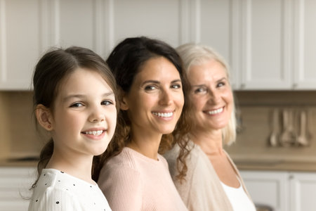 Happy cute little tween child girl, brunette mom and cheerful grandma posing for family shooting,...