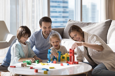 Beautiful family with two adorable kids playing wooden blocks at modern home, laughing, feel happy,...