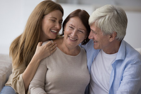 Cheerful adult daughter and senior husband hugging mature mom with love, care, affection,...