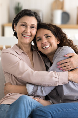 Vertical portrait happy mature 60s mother cuddling tightly with love and tenderness her millennial...
