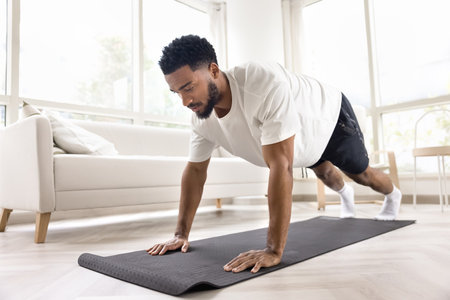 Focused athletic strong African man doing pushups, morning exercises at home, caring for power,...