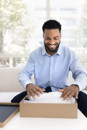 Joyful positive Black client man getting parcel from transportation logistic service, touching...