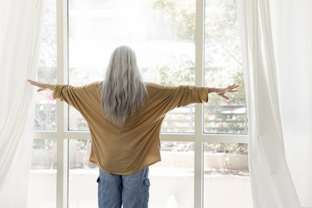 Back view of senior woman with long naturally grey hair in casual opening drapes, parting white...