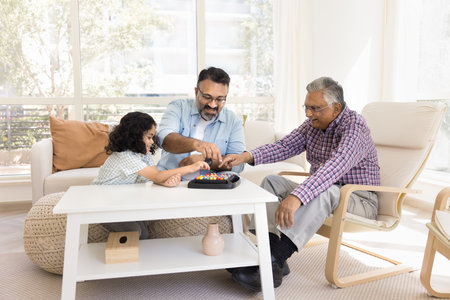Cheerful Indian senior grandads and little granddaughter girl playing with colorful balls at home,...