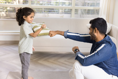 Positive strong Indian dad training little daughter kid, teaching boxing, showing fist work. Cute girl and young father exercising at home together, learning martial arts, fightingの写真素材