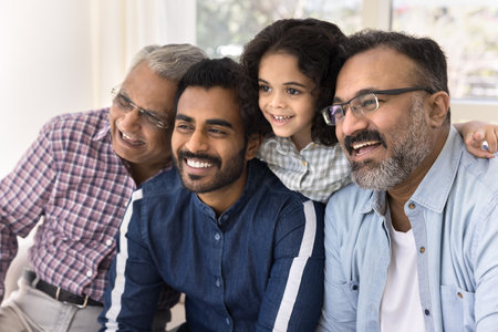 Happy Indian family four generations meeting and laughing, posing at home, looking away with toothy smiles, laughing. Kid, dad, granddad, great grandpa family portraitの写真素材