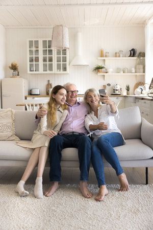 Cheerful pre-teen girl spend leisure time with mature mother and grandfather at home, look at...