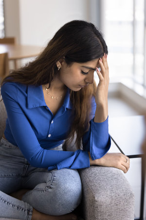 Frustrated tired young Indian woman feeling bad, stressful, upset, touching head, forehead with...