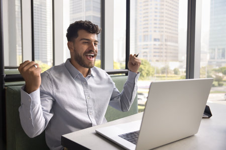 Happy joyful Arab business man enjoying win, victory, achieving job success, making winner yes hands...
