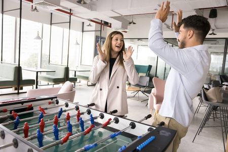 Couple of happy excited office employees giving high five over corporate board game, playing table...