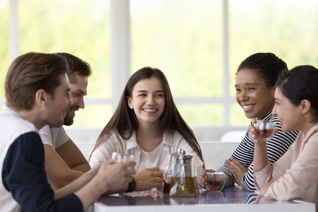 Diverse team of cheerful happy friends chatting and laughing in cafe, drinking tea at table in...