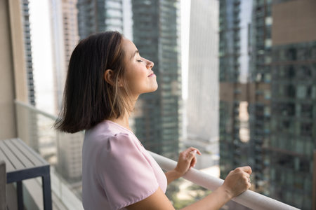 Happy peaceful young tourist woman enjoying big city view from skyscraper building balcony,...