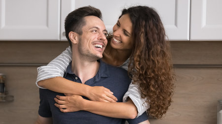 Loving Hispanic spouses spend time together in renovated modern kitchen, loving wife snuggle tightly...