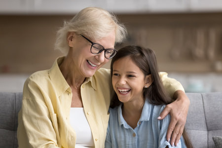 Cheerful blonde mature grandma in glasses hugging happy grandchild girl with love, care, smiling, laughing, talking to kid, having fun, enjoying being grandmother, family relationshipの写真素材