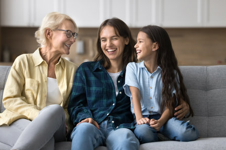 Happy child, mother and grandmother meeting at home, talking and laughing on comfortable couch, hugging with love, warmth, care, enjoying family relations, communicationの写真素材