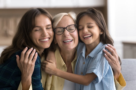 Happy sweet loving granddaughter kid and young mom hugging grandma with closed eyes and head touches, smiling, celebrating mothers day, enjoying close family relationshipsの写真素材