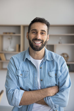 Happy handsome young Hispanic businessman in casual standing with arms folded, looking at camera with toothy smile. Young startup owner, entrepreneur man, business professional vertical portraitの写真素材