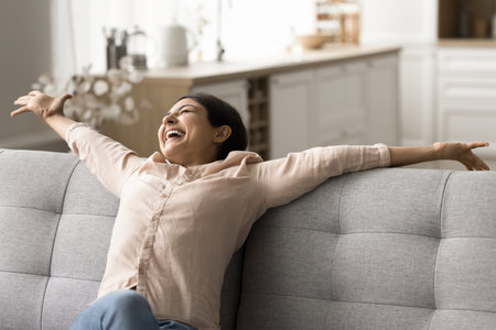 Woman relaxing on comfortable modern new bought couch, stretch her body, feels happy spend time on cozy sofa at own or rented apartment on vacation. Furnishing store advertisement, carefree day-offの写真素材