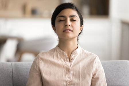 Young serene Indian woman meditates with eyes closed to boost state of inner peace, mindfulness and self-awareness, female enjoy moment of tranquillity, relaxing, focusing on her thoughts, quiets mindの写真素材